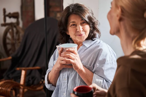 Elderly woman smiling to her young teacher and listening her while drinking coffee — ストック写真