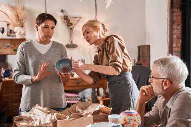 Öğretmen, gazetede el yapımı tabakları paketlerken üst düzey müşterisiyle konuşuyor.