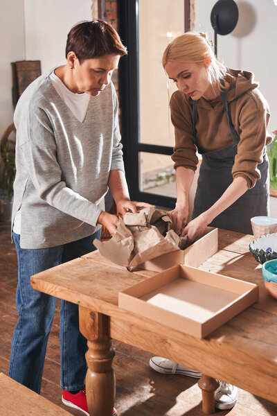 Female teacher showing to her senior client how to wrapping handmade plates at the paper