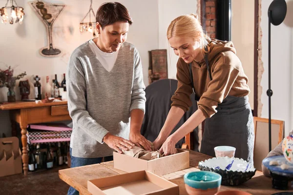 Femme âgée et son professeur concentré emballant des assiettes aux boîtes de placard — Photo