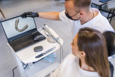 Doktorun dişlerini beyazlatırken dizüstü bilgisayara bakan sakin kadının yüksek açılı görüntüsü. Stok fotoğrafı