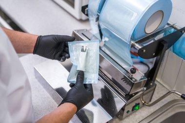 Erkek dişçinin özel paketleri otoklava makinesine yerleştirmeden önce özel paketlere yerleştirirken görüntüsü kesilmiş.