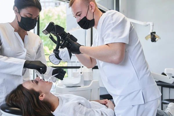 Dentist man photographing teeth before teeth whitening procedure. He working with multiracial nurse. Dental and teeth whitening concept