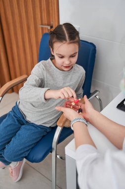 Klinikte tedaviden bahsederken küçük kızın doktorların elinden şekeri alışını yüksek açıdan görüyor. Pediatri konsepti. Stok fotoğrafı