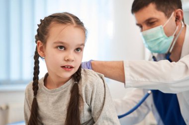 Doktor steteskopla çocuk bir hastayı muayene ediyor. Steteskop tutan ve hastanedeki hasta kızın kalbini dinleyen ilgili bir doktor. Sağlık hizmetleri kavramı