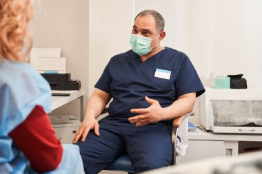 Özel klinikteki randevusunda kadın müşteriyle koruyucu maske takan kıdemli erkek terapist. İyi bir sağlık hizmeti. Sağlık ve Tıp Konsepti