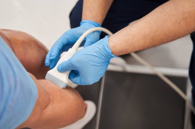 Diz eklem ultrason doktoru kadın hastayı muayene etti. Erkek doktorun kadın bacağına özel bir alet dayadığı görüntüler.