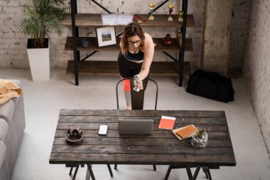 Spor blogcusu. Antrenman için giyinmiş engelli kadının yüksek açılı görüntüsü dizüstü bilgisayarın önünde duruyor ve ödülünü kameraya gösteriyor.