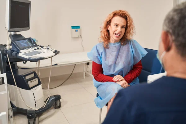 Klinikteki doktorunu ziyaret eden gülümseyen bir kadın. Sağlık kontrolü yaparken hastayı dinleyen kıdemli erkek uzman. Tıp konsepti