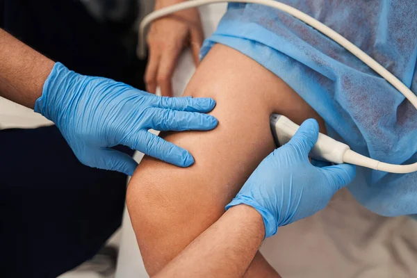 Kıdemli doktorun hastanede kadın bacaklarına ultrason çekerken görüntüsü kesilmiş. Erkek doktor hastasının ultra sesini çıkarıyor.