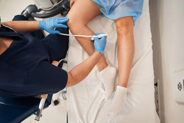 High angle view of the orthopedist doctor doing ultrasound examination of patients leg veins in his office. Young woman passing ultrasound scan in clinic. Medical research concept