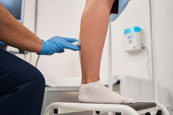 Cropped view of the doctor doing ultrasound examination of patients leg veins in his office. Young woman passing ultrasound scan in clinic. Medical research concept