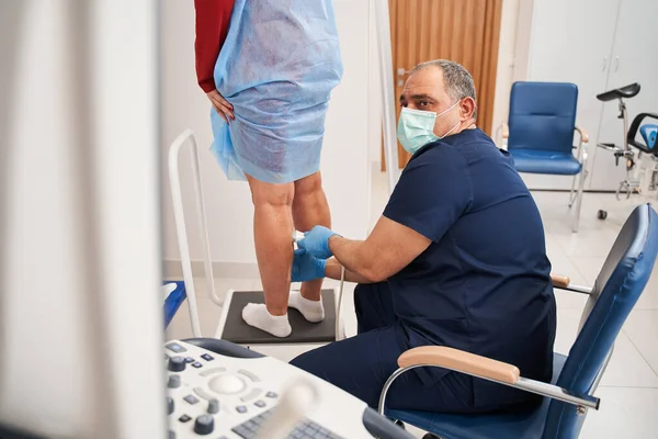 Hastanedeki ekrana bakarken kadın hasta bacağına ultrason uygulayan olgun bir doktor. Stok fotoğrafı