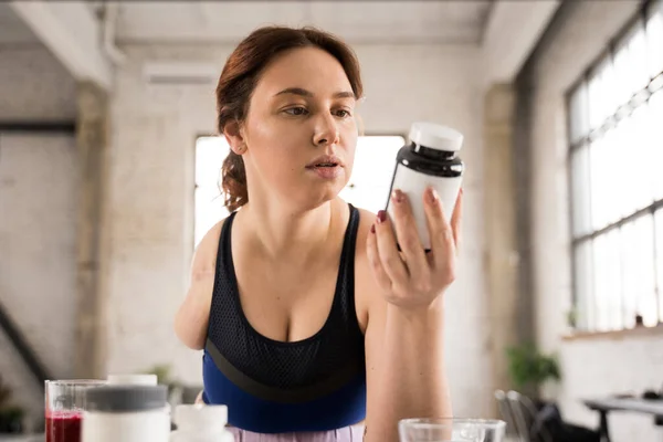 Low angle view of the woman without hand holding jar with supplements and looking at it with interest. Nutrition and medicine concept