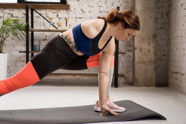 在家里锻炼时 手臂被截肢的妇女会让肌肉暖和起来 站在瑜伽垫旁边的女性侧视图 — 图库照片