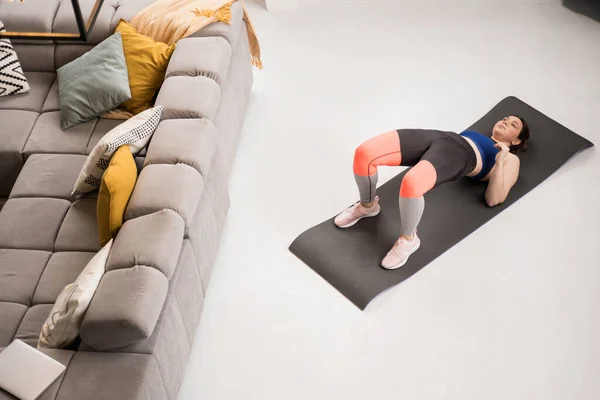 High angle view of the woman without hand raising up her legs while pumping her buttocks at the yoga mat. Sport and recreation concept
