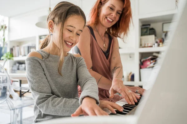 Low angle view of the mom teaches her little daughter to play the piano. They are having fun and laughing. Family and maternity concept