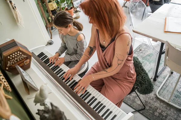 Caucasian woman sitting at the piano and playing song together with her little daughter. Family and maternity concept. Stock photo