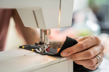 Close up of hands of clothes designer. Skilful woman sews a cloth with the help of sewing machine while spending time at home