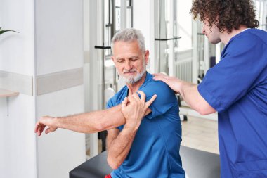 Senior in recovery doing exercises, having massage from skilful doctor. Therapist helping to old man with back in medical rehabilitation and physical therapy centre
