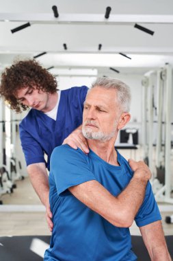 Senior patient sitting during the massage session while sitting at the bench. Recovery at the retirement age concept