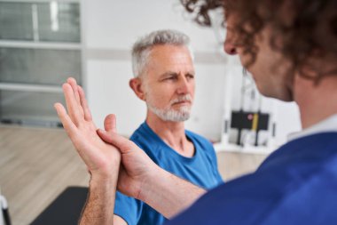 Cropped view of the chiropractor giving help to senior man with arm pain for physical recovery. Orthopaedic stretching hand and shoulder of elder patient with injury for physiotherapy