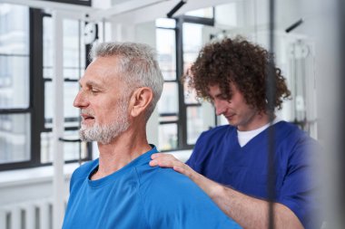 Osteopathy assistant stretching back and shoulder of patient with muscle pain for physiotherapy. Chiropractor treating senior man with injury, helping with physical recovery and remedy