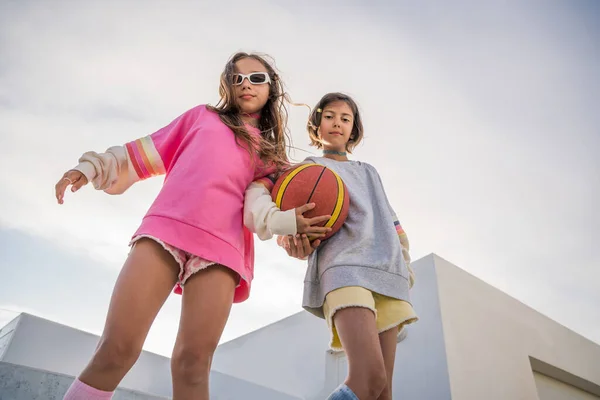 Low angle view of the positive pretty girls in vivid clothes looking at the camera while playing on the playground. Stock photo