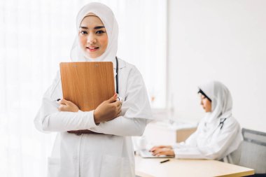 Profesyonel tıp. Steteskoplu, üniformalı, hastane masasında dizüstü bilgisayarla çalışan iki Müslüman kadın doktor. Sağlık ve tıp.