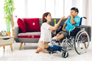 Mutlu aşk portresi. Asyalı anne oynuyor ve bakıcı tekerlekli sandalyede oturan engelli çocuğa bakıyor. Evde engelli bakımı konseptinde iyi vakit geçiriyor.