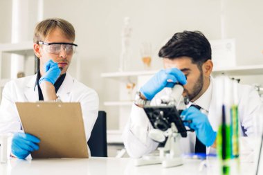 Profesyonel iki bilim adamı test tüpünde sıvı analiz ederken ve karıştırırken kimyasal bir deney yapıyor. Genç bilim adamı laboratuvarda cam üzerine kimyasal örnekler bırakıyor.