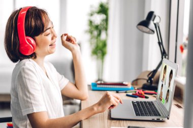 Kulaklıklı kadın öğretmen, çevrimiçi eğitim e-öğrenim sistemi öğretiyor ve laptop bilgisayarına bakıyor. Bir grup öğrenci video konferansında ev ödevi hakkında bilgi ediniyor.
