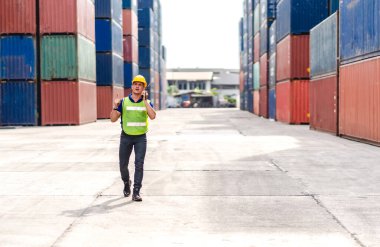 Kasklı profesyonel mühendis konteynır ustabaşı ayakta çalışıyor ve telsiz kullanıyor. Stokları yükleme için konteynıra koyuyor. Lojistik ulaşım ve iş sektörü ihracatı