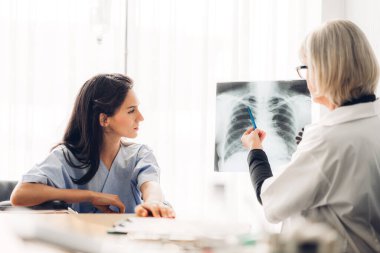 Steteskoplu üniforma giyen kıdemli kadın doktor, akciğer zatürresi olan hastanın göğüs röntgeni görüntülerini tarayıp incelemeye yardımcı oluyor.