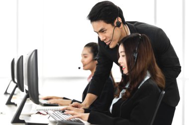 Mutlu Asyalı gülümseyen çağrı merkezi işletme operatörü grubu, çağrı merkezindeki masaüstü bilgisayarında çalışan ve kulaklıkla konuşan ekip telefon hizmetlerini desteklemeye yardımcı olur.