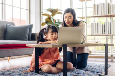 Mother and asian kid little girl learning and looking at laptop computer making homework studying with online education e-learning system.children video conference with teacher tutor at home