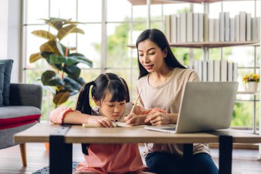 Mutlu bir aşk portresi. Asyalı bir anne, küçük kızı Asyalı 'ya laptopta öğrenme ve öğrenim öğretiyor. Anne ve Asyalı kız, evde ev okulunda kitap ve kalemle ödev yazıyorlar.