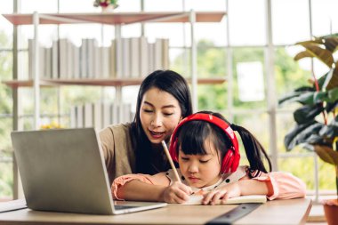 Mutlu bir aşk portresi. Asyalı bir anne, küçük kızı Asyalı 'ya laptopta öğrenme ve öğrenim öğretiyor. Anne ve Asyalı kız, evde ev okulunda kitap ve kalemle ödev yazıyorlar.
