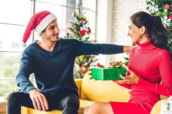 Noel Baba şapkalı romantik çift Noel ağacını süslerken ve yeni yılı kutlarken gülümserken ve birlikte vakit geçirirken eğleniyor. Adam kadınlara hediye kutusu sürprizi yapıyor.