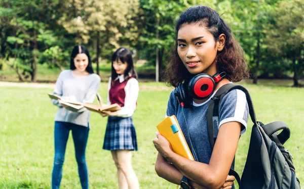 笑顔の女子留学生やティーンエイジャーが立ち上がり 大学の公園で学生のグループとカメラを見て本を保持します 教育と友情コンセプト — ストック写真