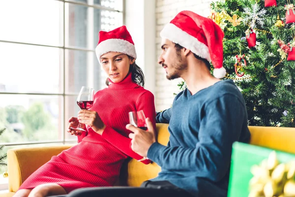 サンタの帽子のロマンチックな甘いカップルは 楽しいとワイングラスを飲みながら新年の前夜を祝い 自宅でクリスマスの時間に一緒に過ごすことを楽しんでいます — ストック写真