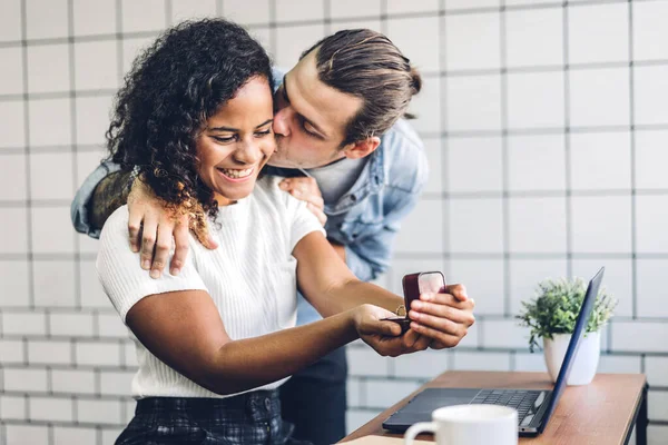 Young handsome man giving ring for surprise to girlfriend and talking together sitting in living room at home