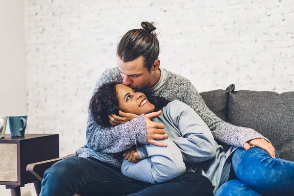 Romantik, genç, mutlu aşk çifti Kafkasyalı erkek ve Afrikalı Amerikalı kadın gülümseyip sevgililer gününde evde yatakta kucaklaşırken eğleniyorlar.