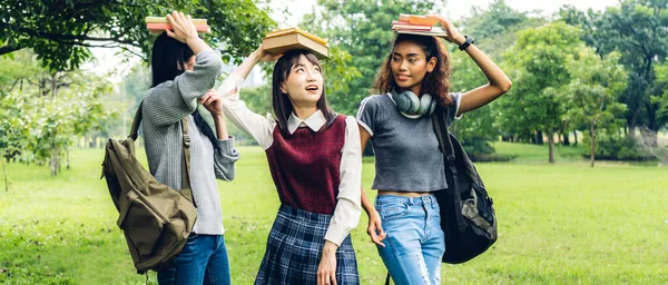 Smiling woman international student or teenager standing and holding book look at camera with group of student in park at university.Education and friendship Concept