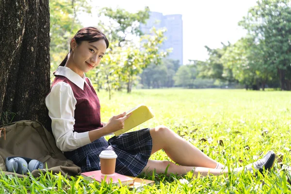 美学生や十代のアジアの女性の肖像は 大学で公園に座っている間 紙の本の仕事の研究とページ雑誌を見て学ぶ読みます — ストック写真