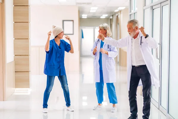Professional medical doctor team with stethoscope in uniform discussing and dancing with happy patient woman with cancer cover head with headscarf of chemotherapy cancer in hospital.health care