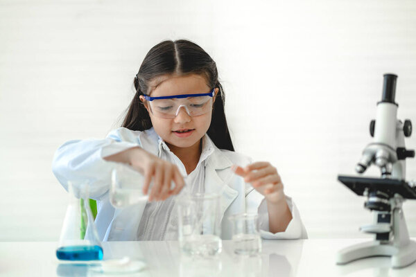 Cute little girl student child learning research and doing a chemical experiment while making analyzing and mixing liquid in glass at science class in school.Education and science concept