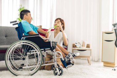 Asyalı fizyoterapistin portresi engelli çocuk sağlığı sorununa rehabilitasyon kliniğinde tekerlekli sandalyede oturarak yardım ve oyun oynayarak yardımcı oluyor.