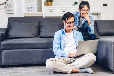 Genç Asyalı çift dizüstü bilgisayarlarını kullanarak rahatlıyor ve çevrimiçi görüntülü konferans görüşmeleri yapıyor. Yaratıcı serbest iş ortakları ev planlaması ve beyin fırtınası yapıyor.