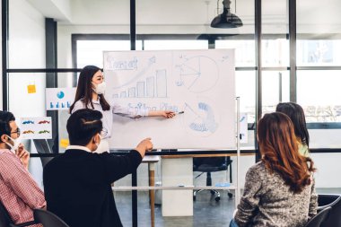 Koronavirüs için karantinada bir grup profesyonel iş toplantısı. Sosyal mesafeli koruyucu maske takıyorlar. Ofiste dizüstü bilgisayarla yaratıcı iş planlaması ve beyin fırtınası.